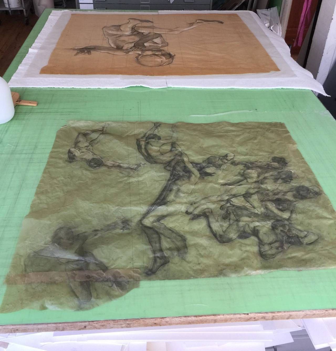 Deux dessins sur papier, marouflés sur tissu, reposent sur une table verte. L'un représente un personnage. L'autre, des personnages en mouvement.