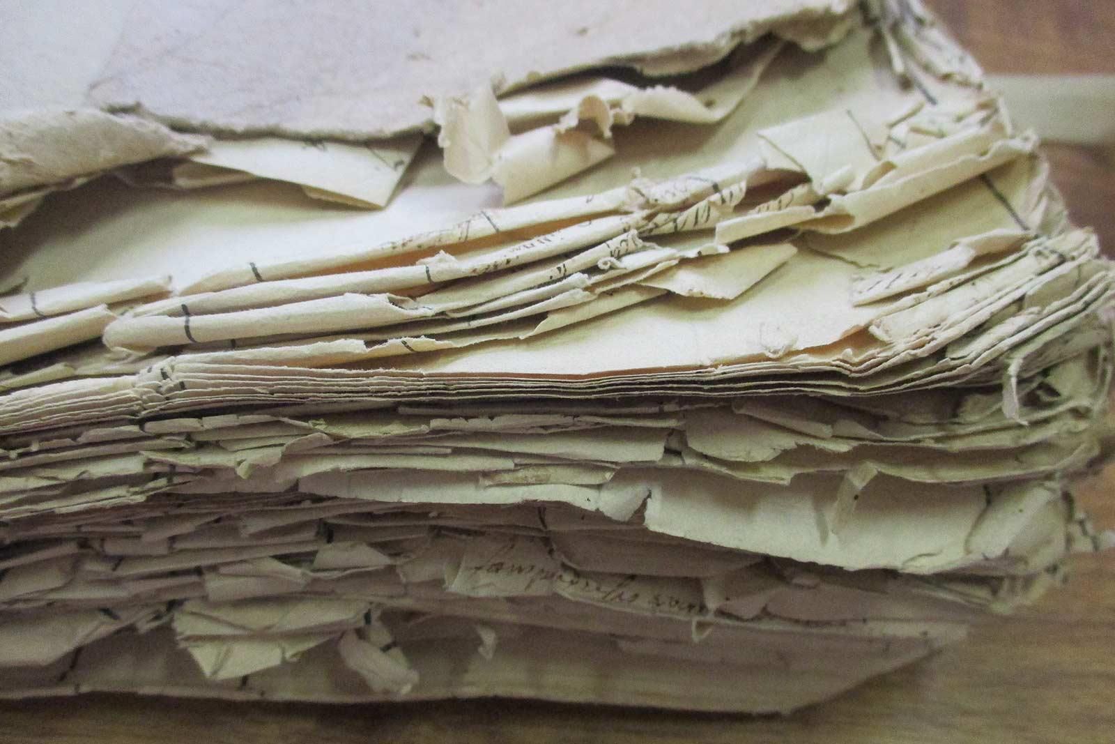 Pile de pages de papier vieillies et déchirées sur une surface en bois.