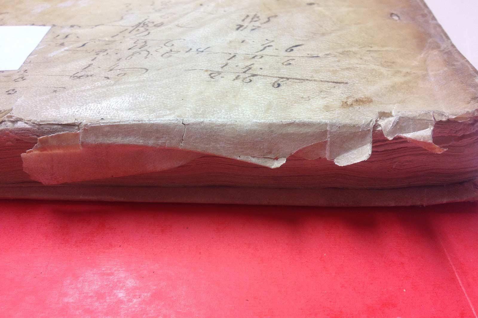 Gros plan sur le dos d'un livre abîmé et vieilli, avec du ruban adhésif transparent déchiré. Surface rouge en dessous.