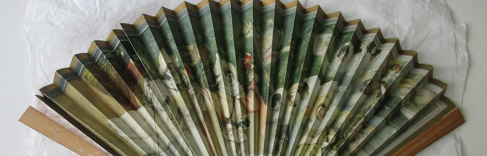 Un éventail pliant peint aux tons verts, beiges et bruns. L'éventail est ouvert.