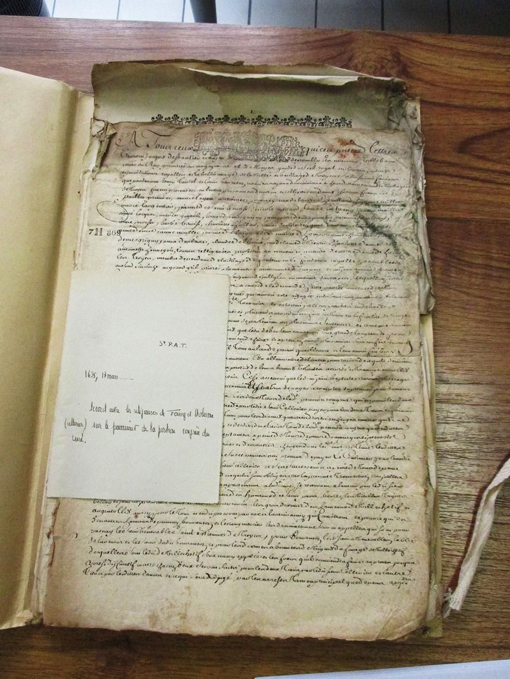 Livre ouvert avec papier vieilli ; texte manuscrit, une note blanche est attachée avec l'écriture.