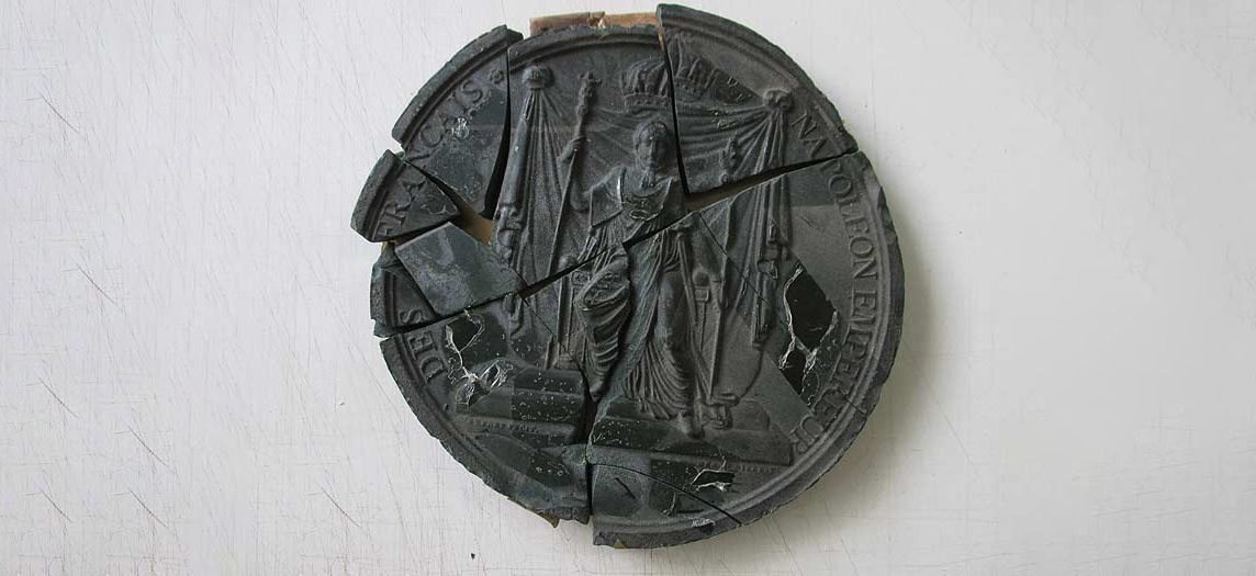 Sceau brisé de couleur foncée avec des figures ou des symboles, un artefact historique.