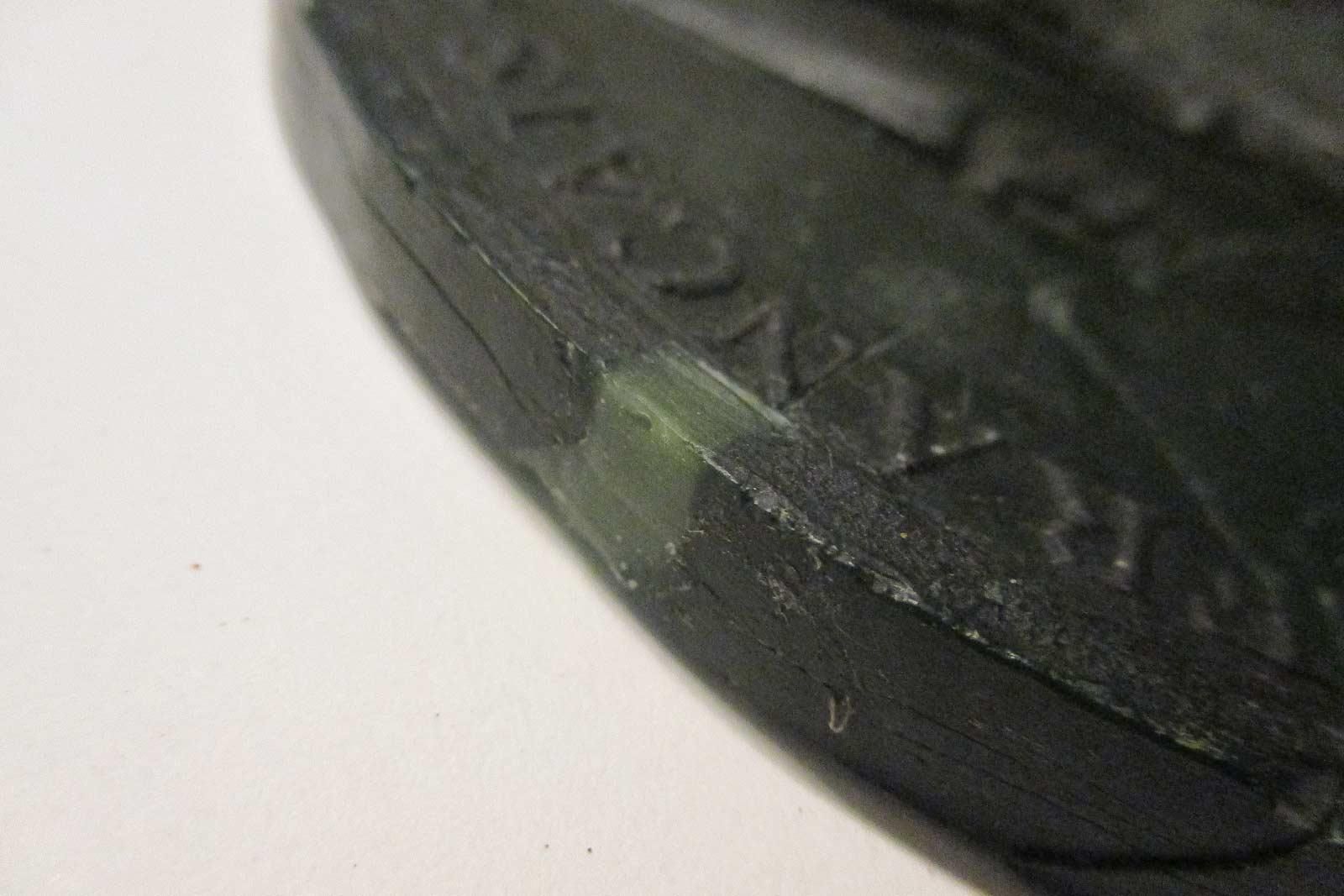 Gros plan sur un sceau sombre et texturé avec un texte gravé ; une petite zone verte est visible.