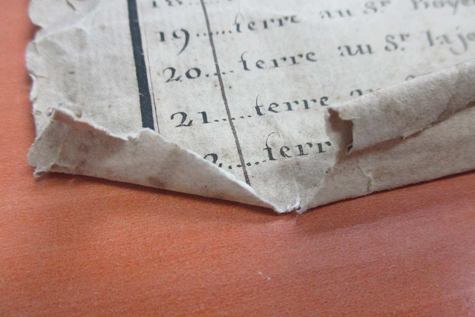 Gros plan sur un papier endommagé et vieilli avec texte français, coin recourbé, reposant sur une surface orange.