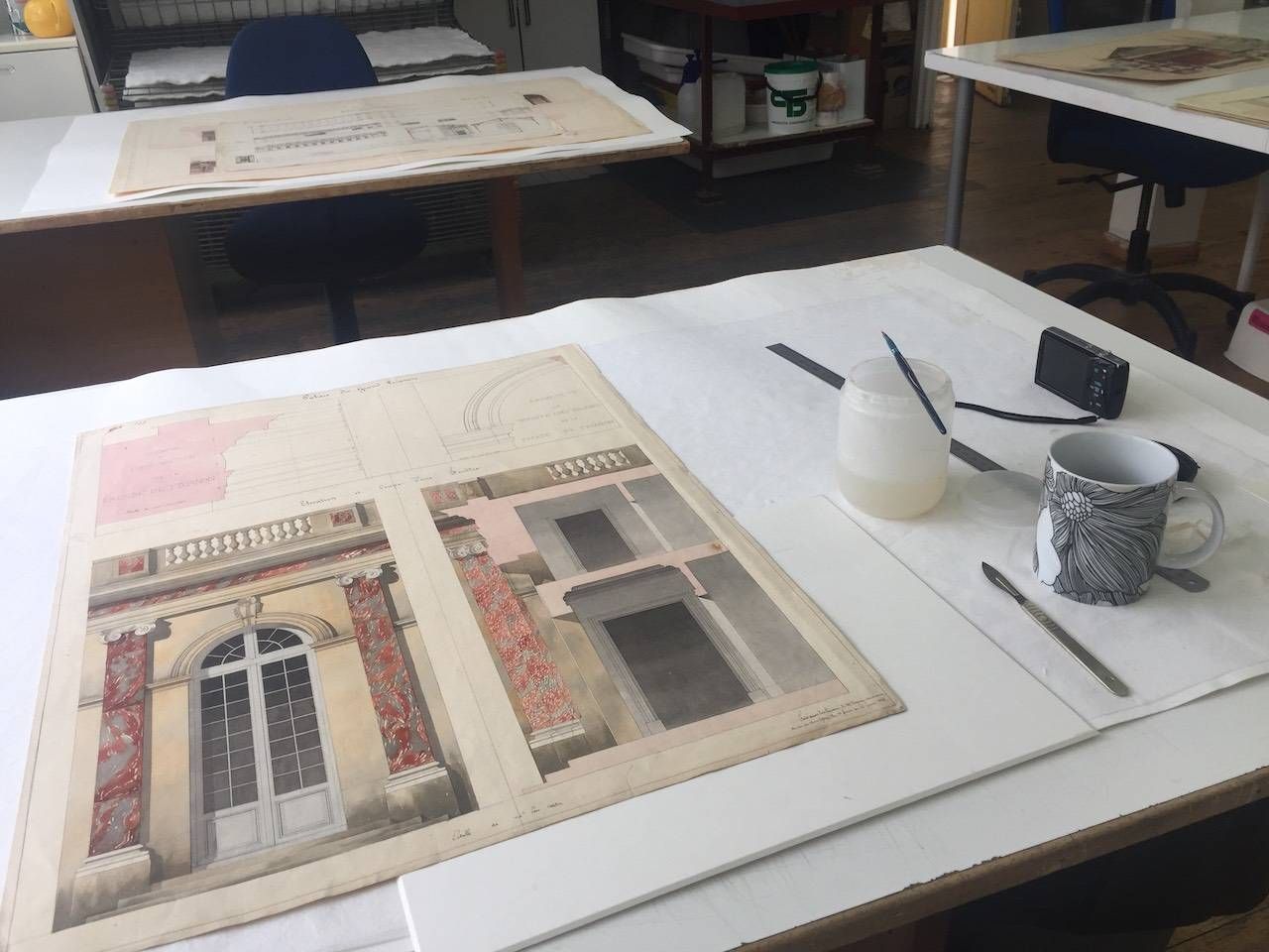 Aquarelles de bâtiments sur une table avec des fournitures d'art dans une salle de travail lumineuse.