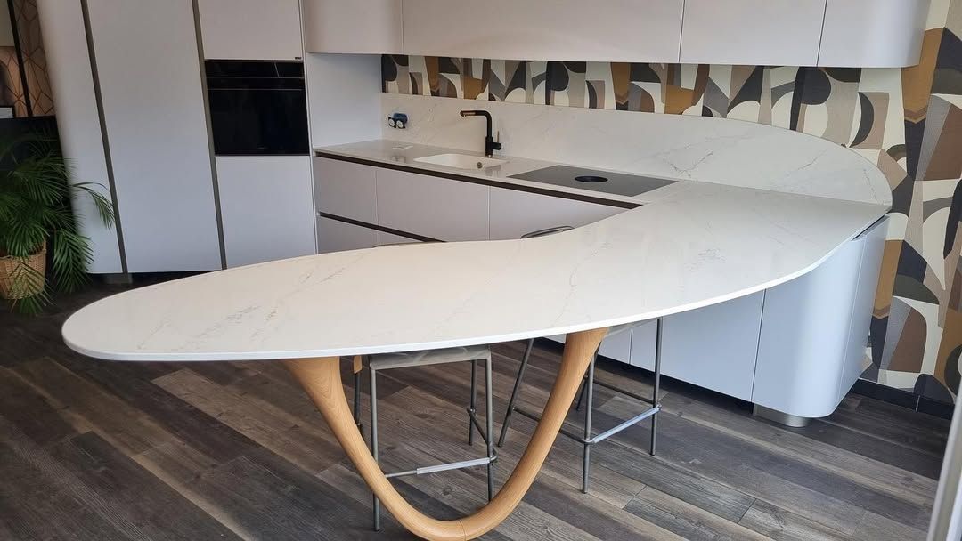 Cuisine moderne avec une table ovale blanche et des pieds en bois incurvés devant un plan de travail et des placards.