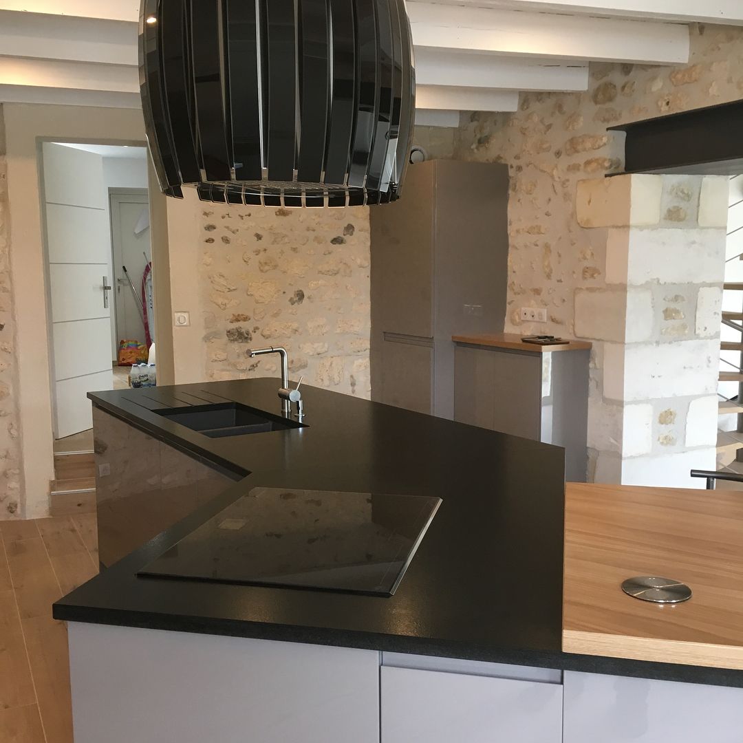 Cuisine moderne en construction avec comptoirs noirs, plaque de cuisson intégrée et murs en pierre