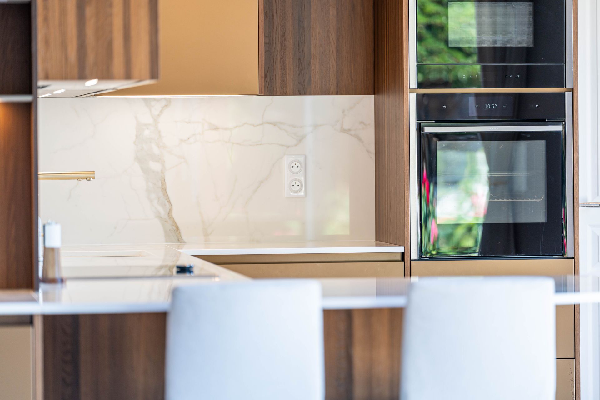 Cuisine moderne avec armoires en bois, crédence en marbre blanc, îlot central et four encastré.
