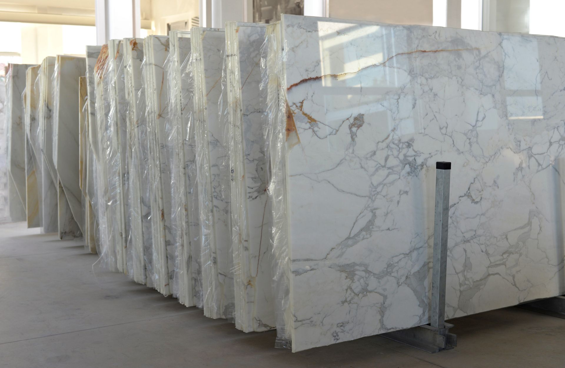 Des piles de dalles de marbre blanc et gris sont stockées verticalement dans un entrepôt ou un dépôt de pierres.