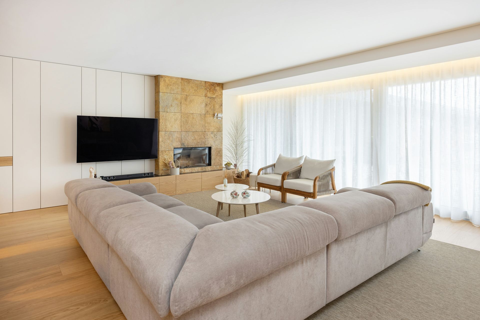Salon moderne avec grand canapé d'angle, télévision, cheminée et rideaux allant du sol au plafond.