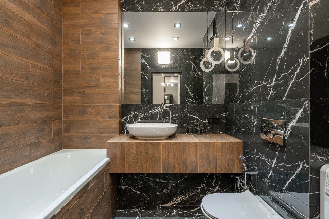 Salle de bains moderne avec finitions en bois et marbre noir, baignoire îlot, lavabo suspendu et grand miroir.