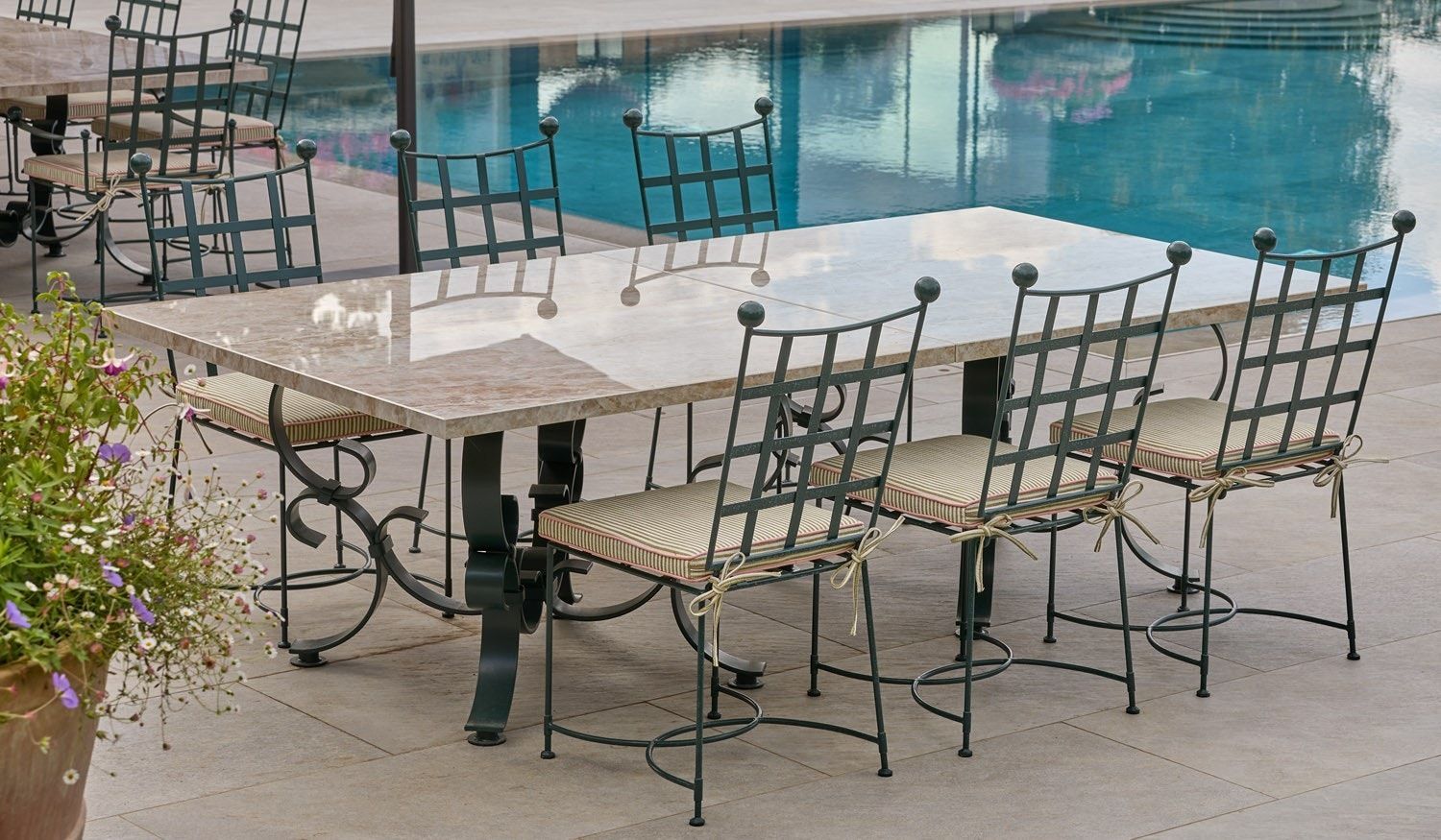 Terrasse aménagée avec chaises et tables en fer forgé, au bord d'une piscine turquoise.