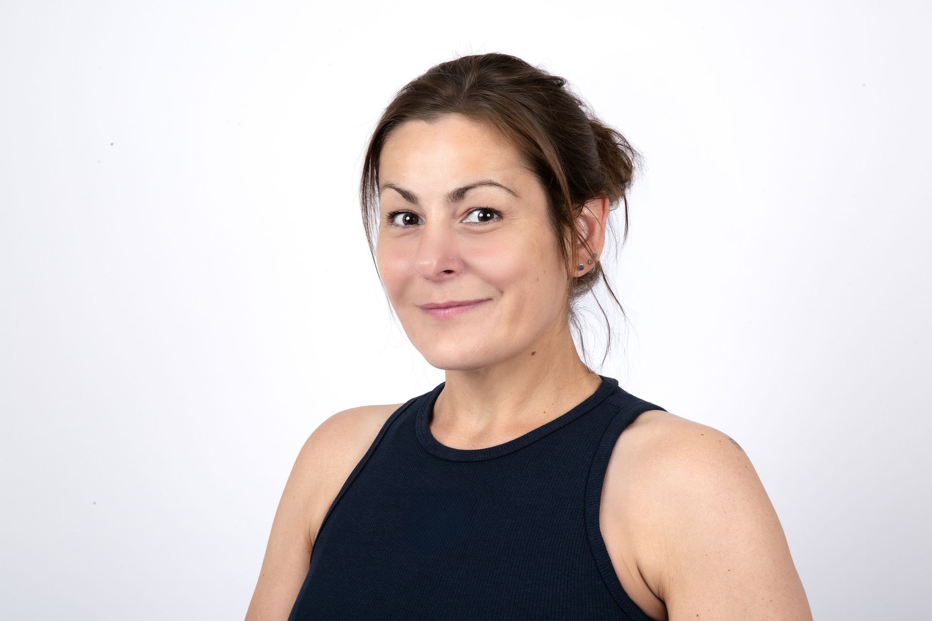 Frau mit dunklem Haar in einem dunkelblauen Tanktop, lächelnd, vor weißem Hintergrund.