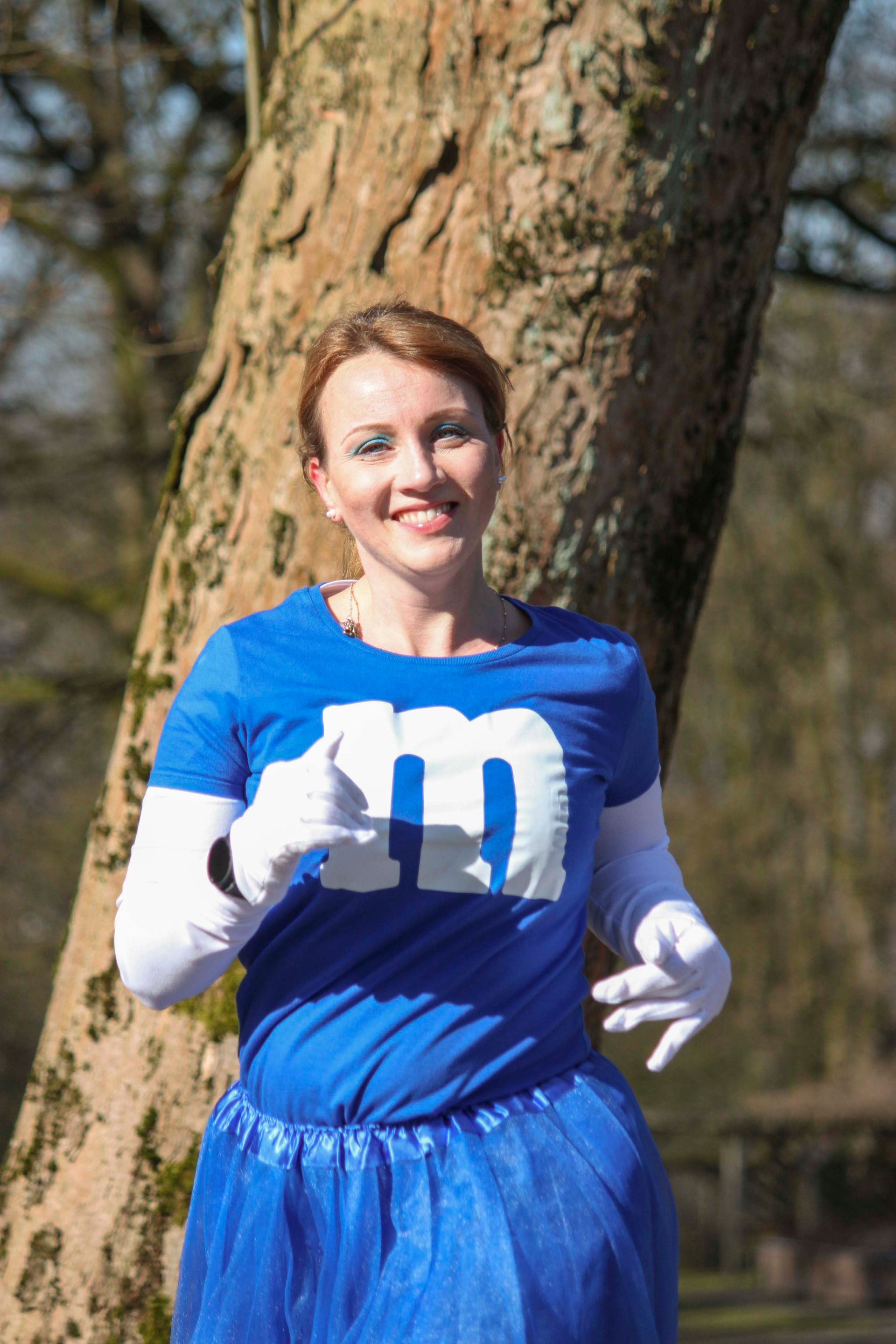 Frau im blauen Kostüm mit „M“ auf dem Hemd, läuft im Freien und lächelt.