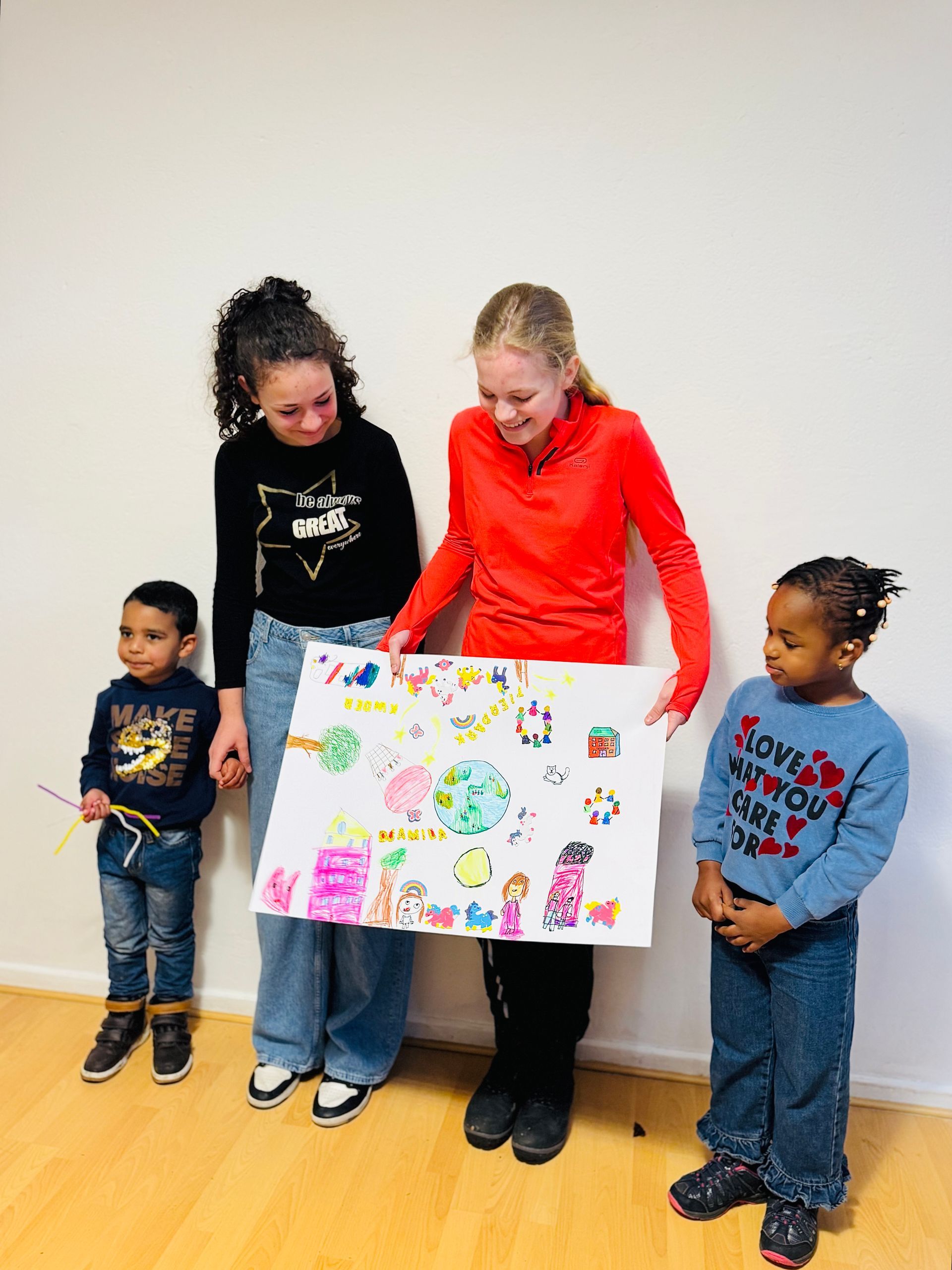 Vier Personen stehen zusammen und halten ein weißes Poster mit bunten, handgezeichneten Illustrationen an eine weiße Wand.