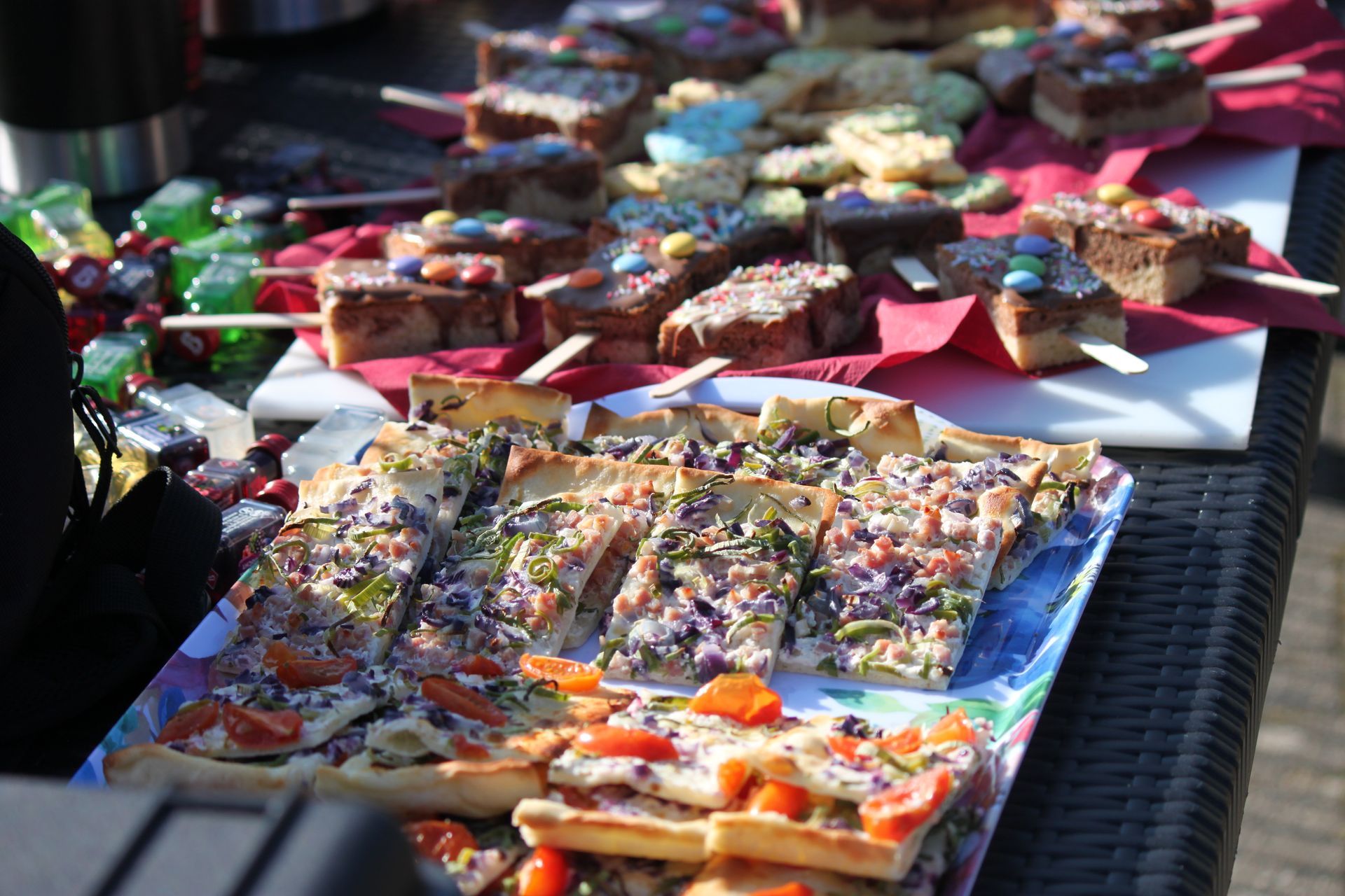 Ein Tisch im Freien mit Snacks: Pizzastücke, Brownies am Stiel und grüne Spieße.
