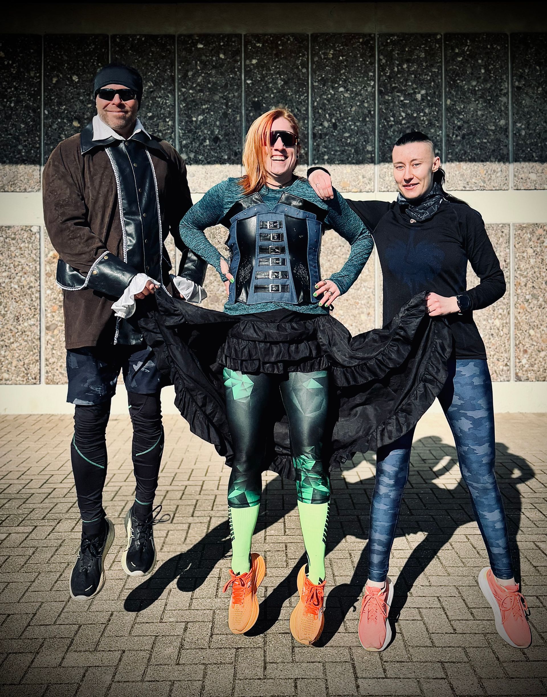 Drei Personen in eklektischen Outfits posieren im Freien. 