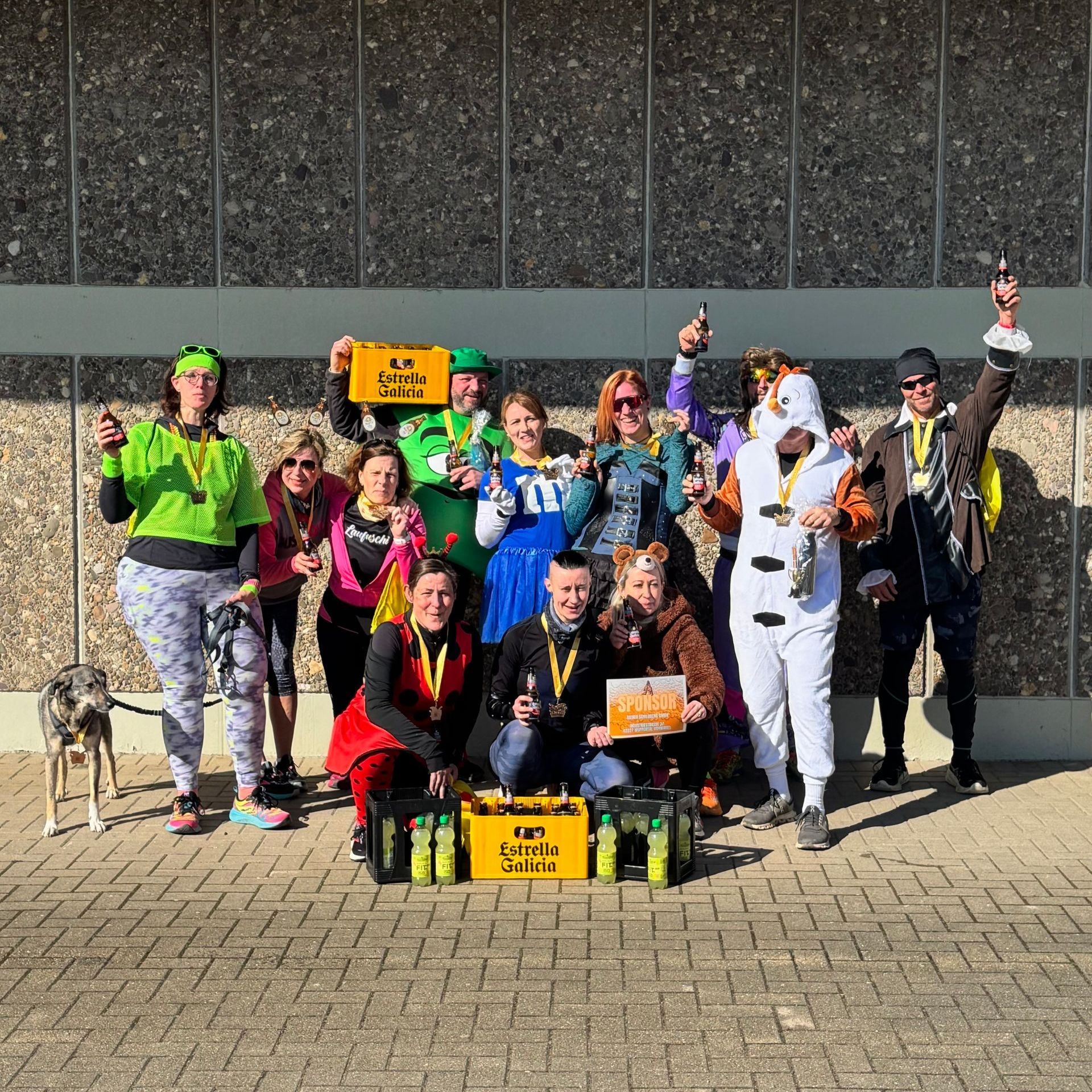 Eine Gruppe kostümierter Menschen feiert mit Bier vor einem Gebäude.