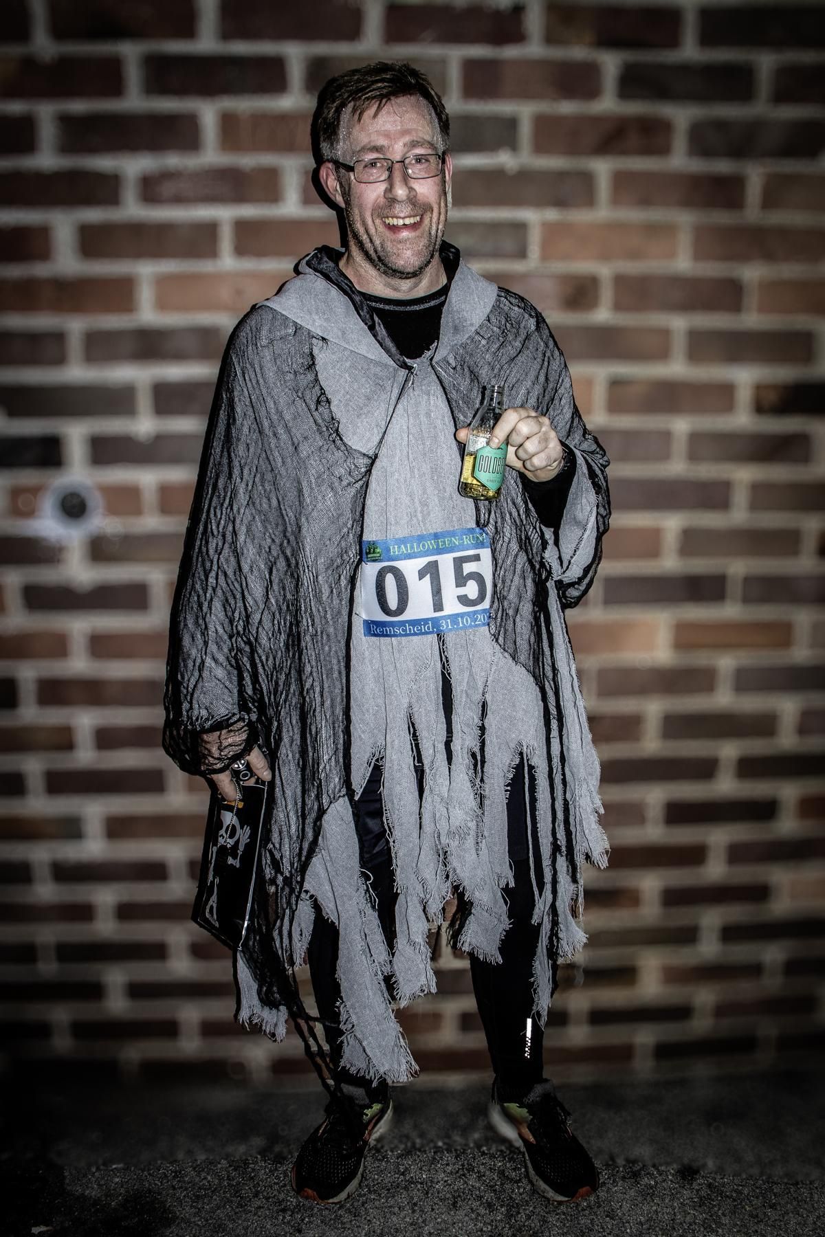 Mann in lilafarbenem Trainingsanzug aus den 80ern, Sonnenbrille und Vokuhila-Perücke zeigt im Freien den Daumen nach oben.
