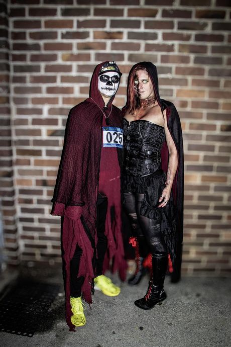 Eine Gruppe von Menschen in unterschiedlichen Halloween-Kostümen posiert nachts auf einem gepflasterten Platz für ein Foto.