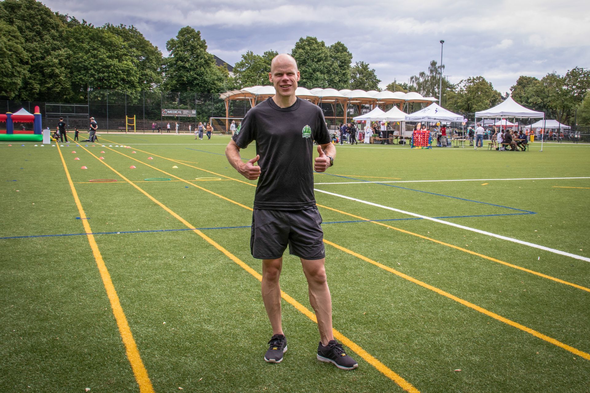 Ein Mann steht auf einem grasbewachsenen Sportplatz; im Hintergrund sind Zelte und Zuschauer zu sehen.