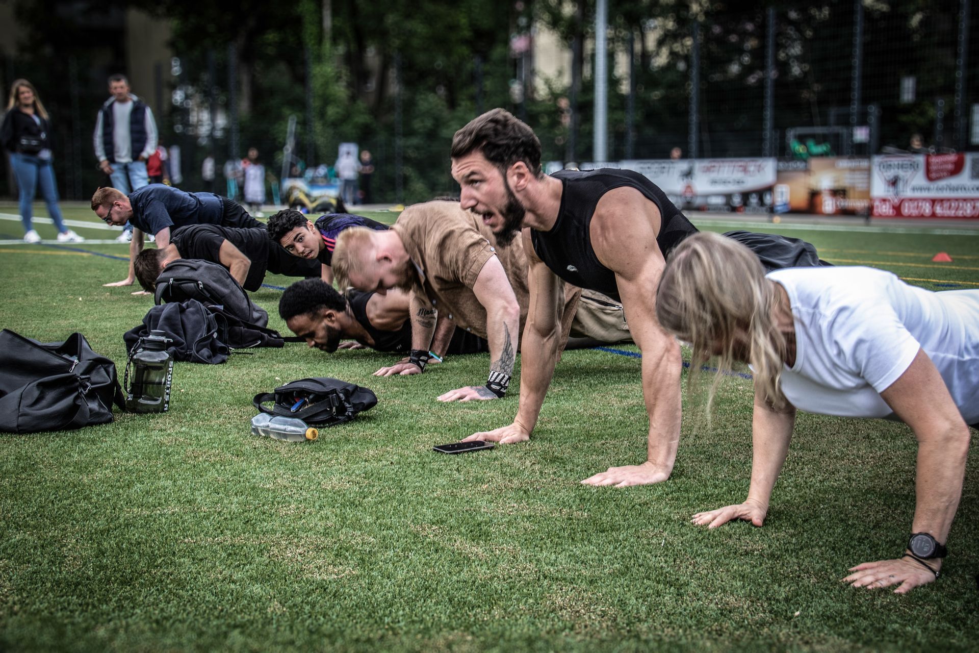 Menschen, die während des Outdoor-Trainings Liegestütze auf einer Rasenfläche machen