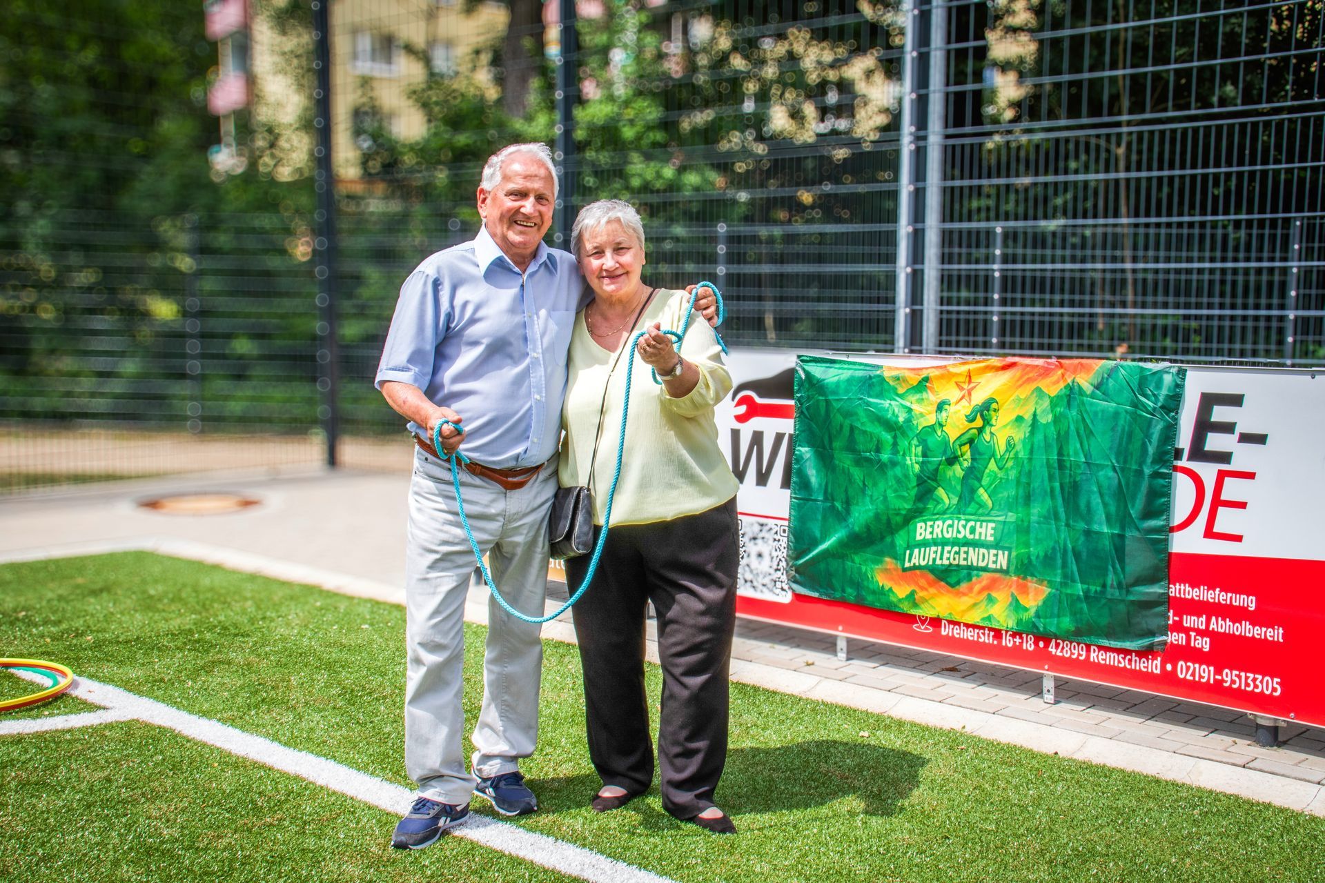 Zwei Personen stehen auf einem Fußballfeld und halten ein grünes Banner an einem Zaun.