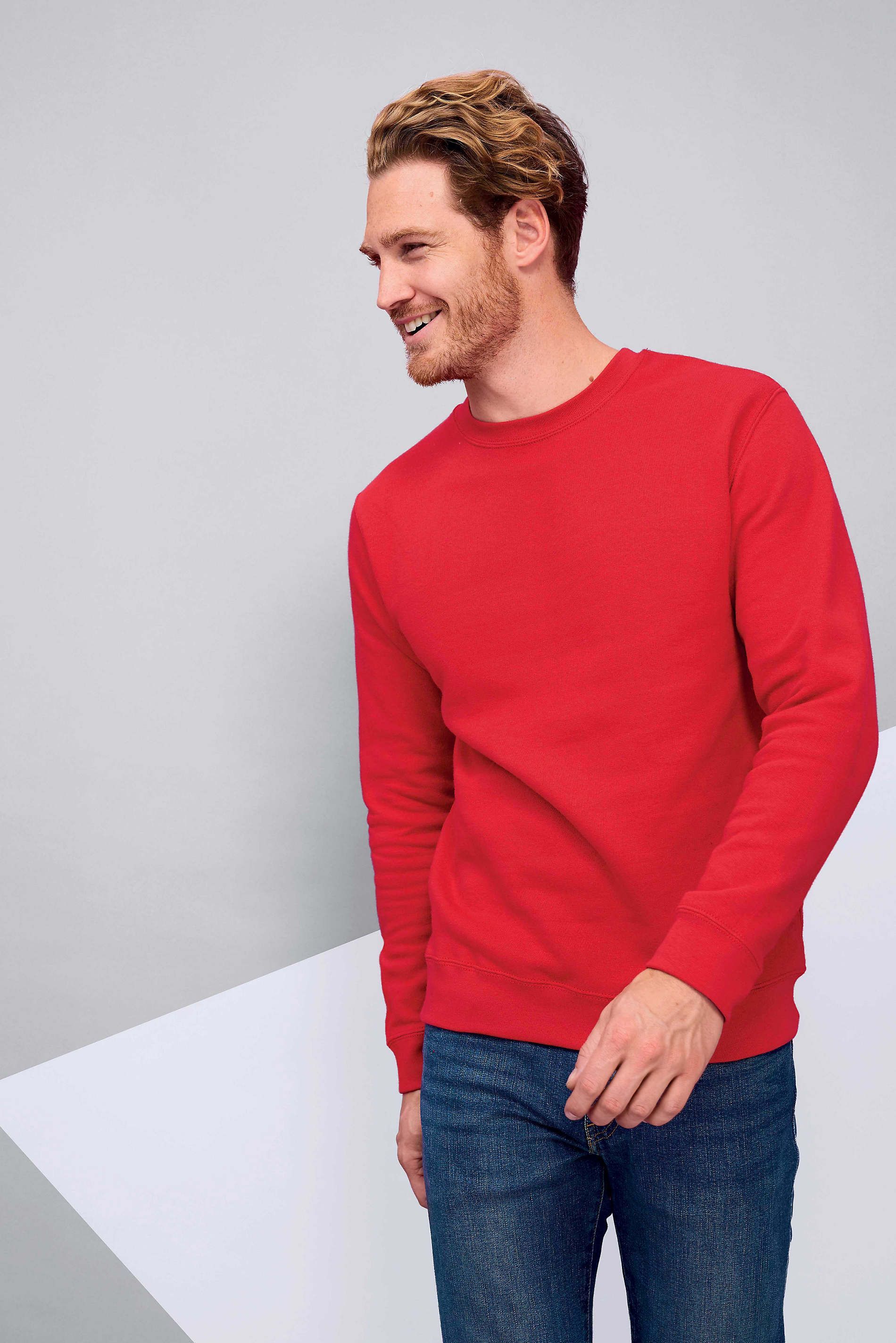 Un hombre lleva un suéter rojo y jeans azules.