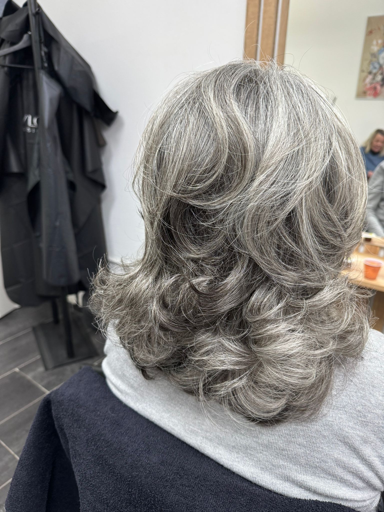 Chioma di lunghezza media e colore grigio con piega ondulata.