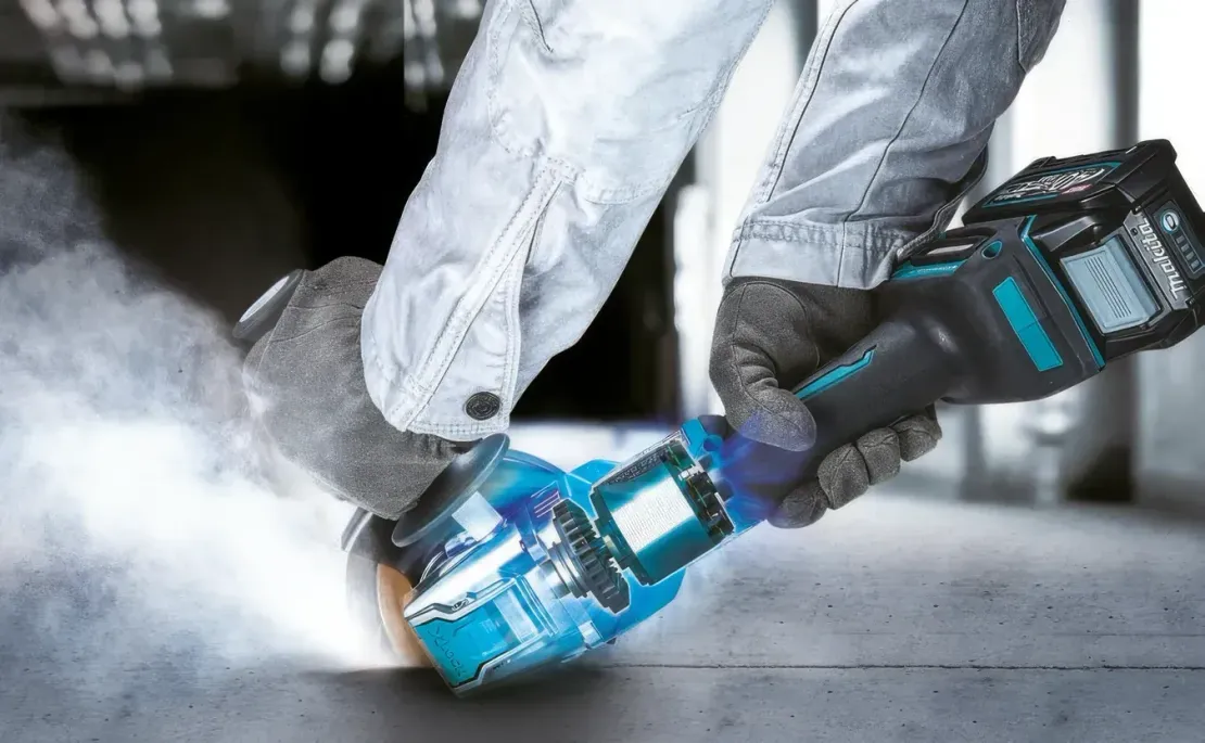 Behandschuhte Hände schleifen einen blau besprühten Gegenstand über den Werkstattboden, Staub und Funken wirbeln auf.