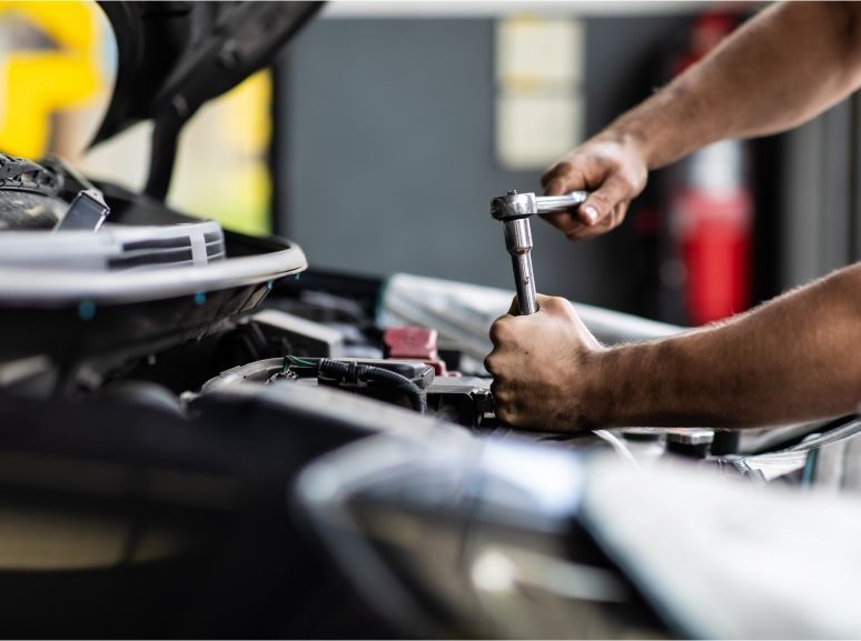 Ein Mann arbeitet mit einem Schraubenschlüssel am Motor eines Autos.