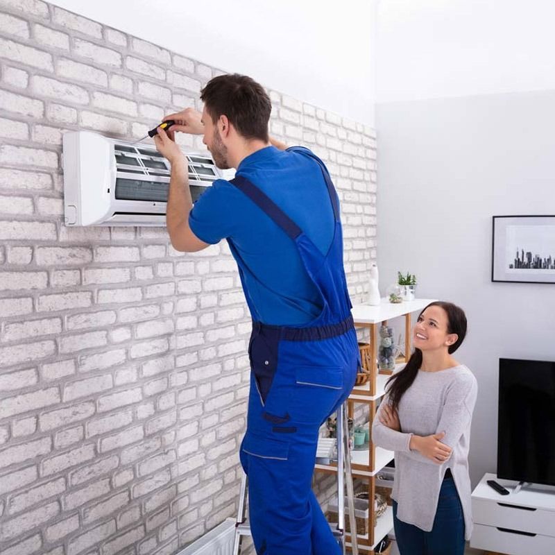 Un hombre está instalando un acondicionador de aire en una pared de ladrillos mientras una mujer observa.