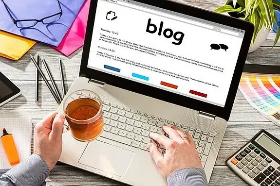 Una persona está escribiendo en una computadora portátil mientras sostiene una taza de té.