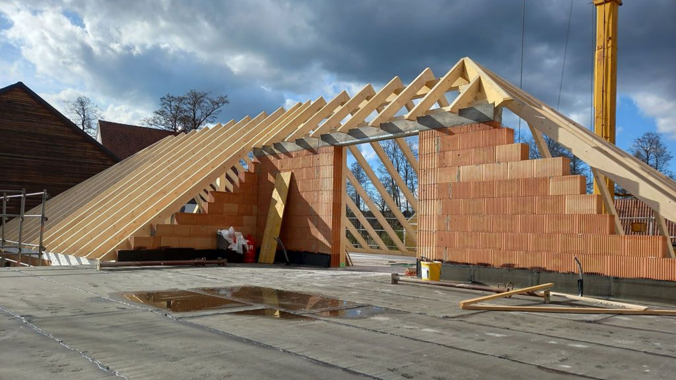 Innenansicht eines im Bau befindlichen Hauses; Holzrahmenkonstruktion mit Betonboden und leeren Räumen.
