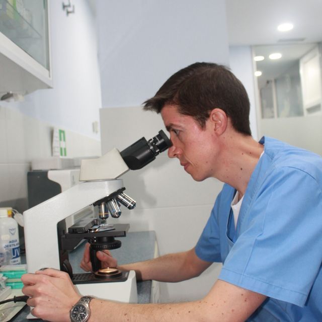 Un hombre con un uniforme azul mira a través de un microscopio.