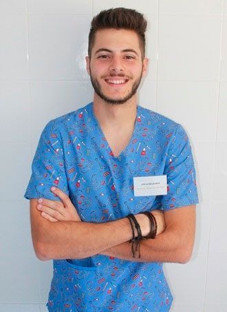 Un joven con un uniforme azul está de pie, con los brazos cruzados y sonriendo.