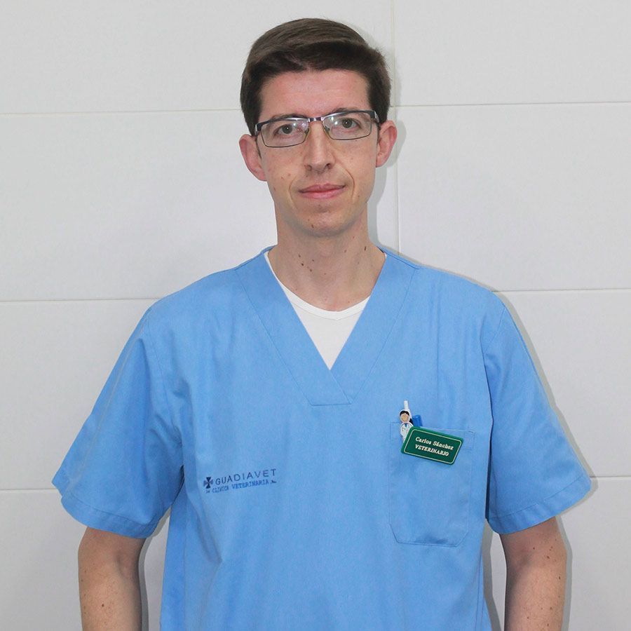 Un hombre que lleva gafas y una camiseta azul está parado frente a una pared blanca.