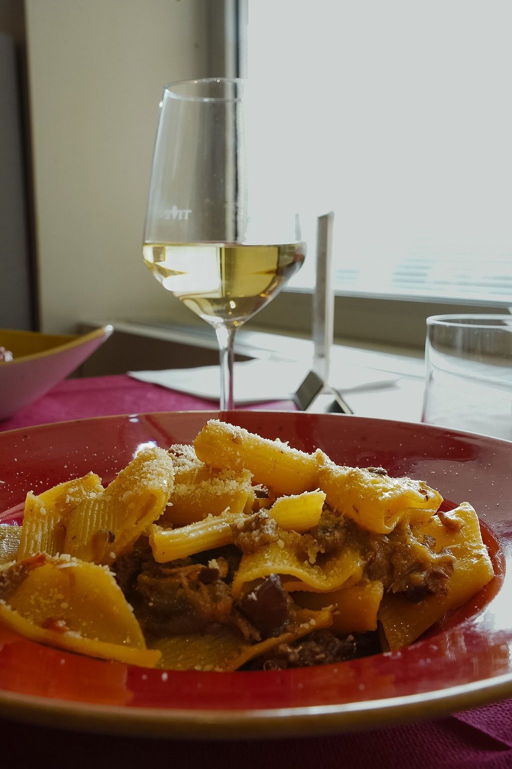 Un piatto di cibo è appoggiato su un tavolo accanto a un bicchiere di vino.