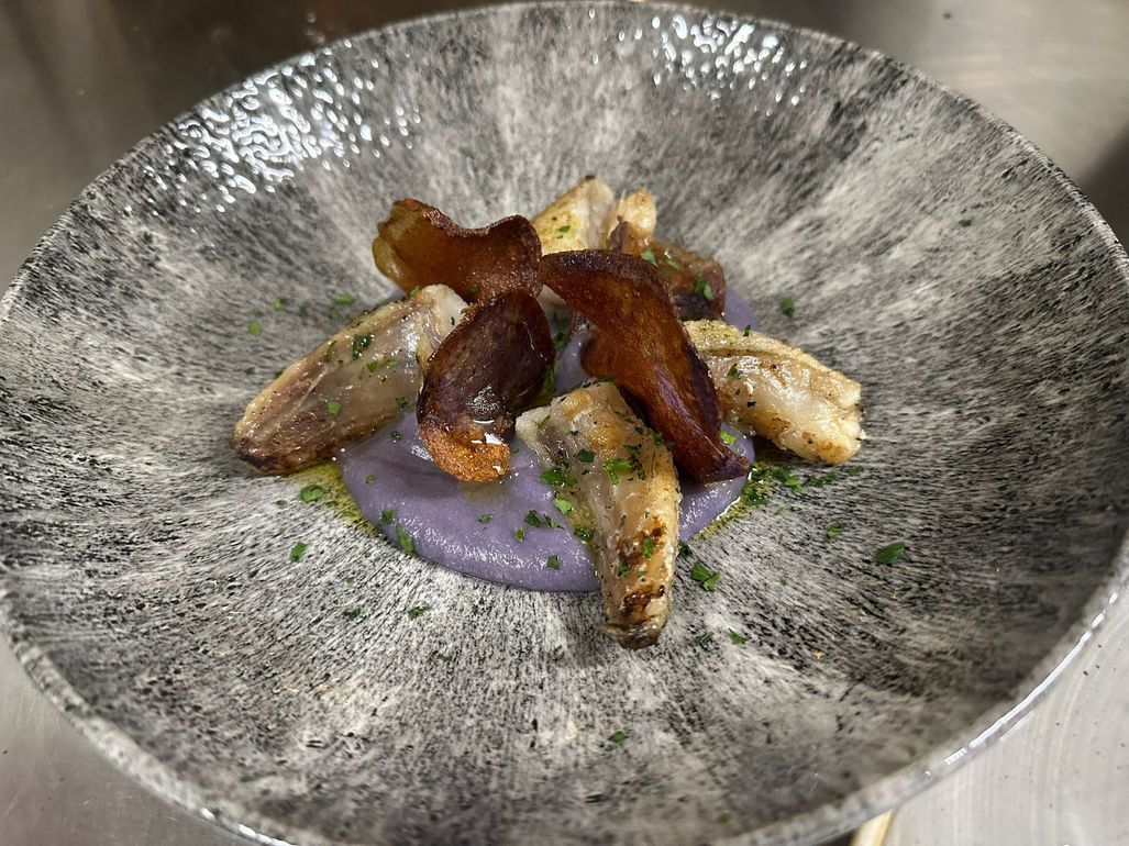 Una ciotola di pasta con olive e capperi su un tagliere di legno.