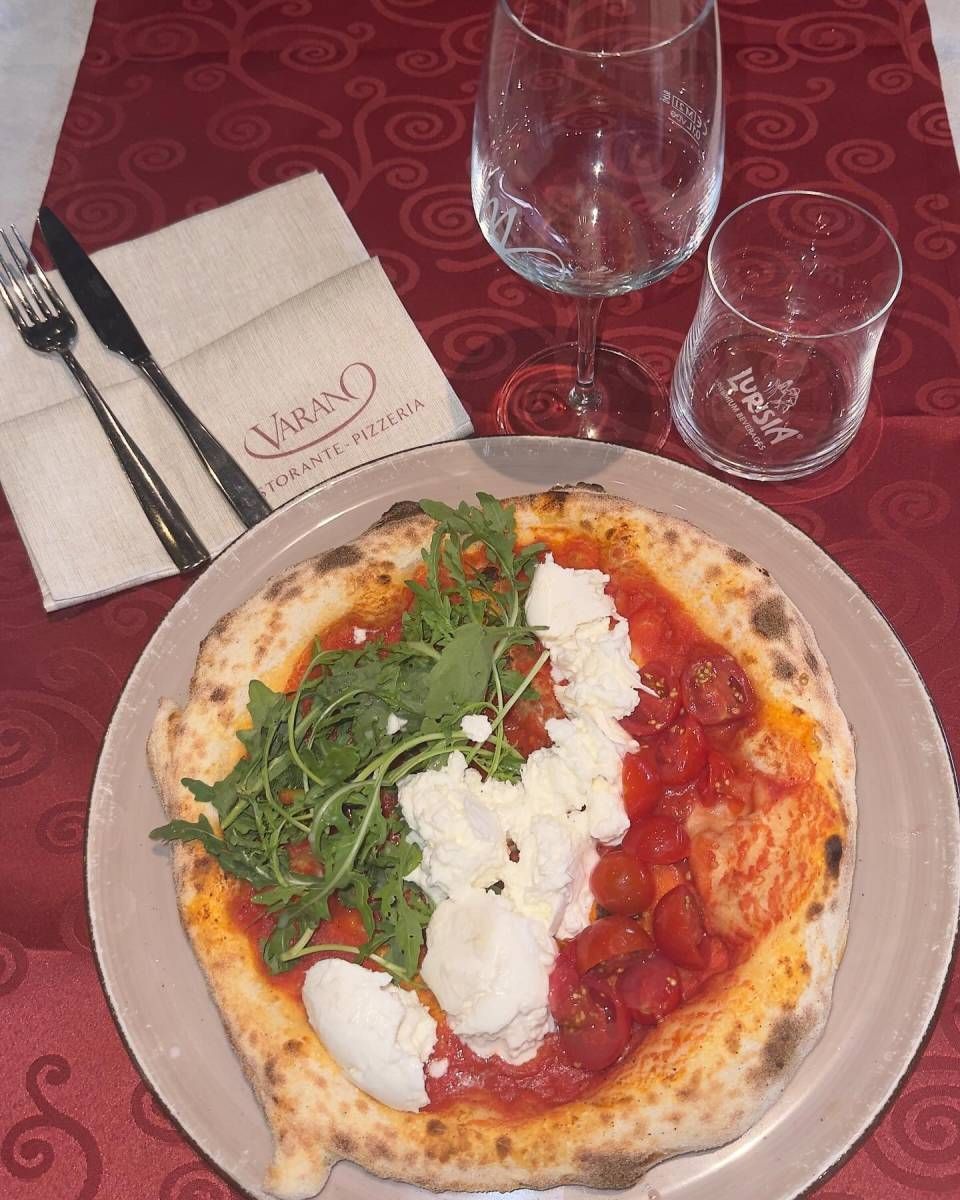 Una pizza su un piatto accanto a un bicchiere di vino