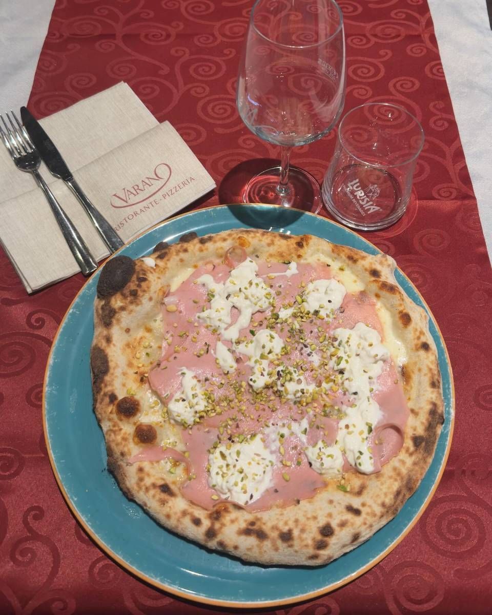Una pizza con mortadella e pistacchio è su un piatto blu su un tavolo