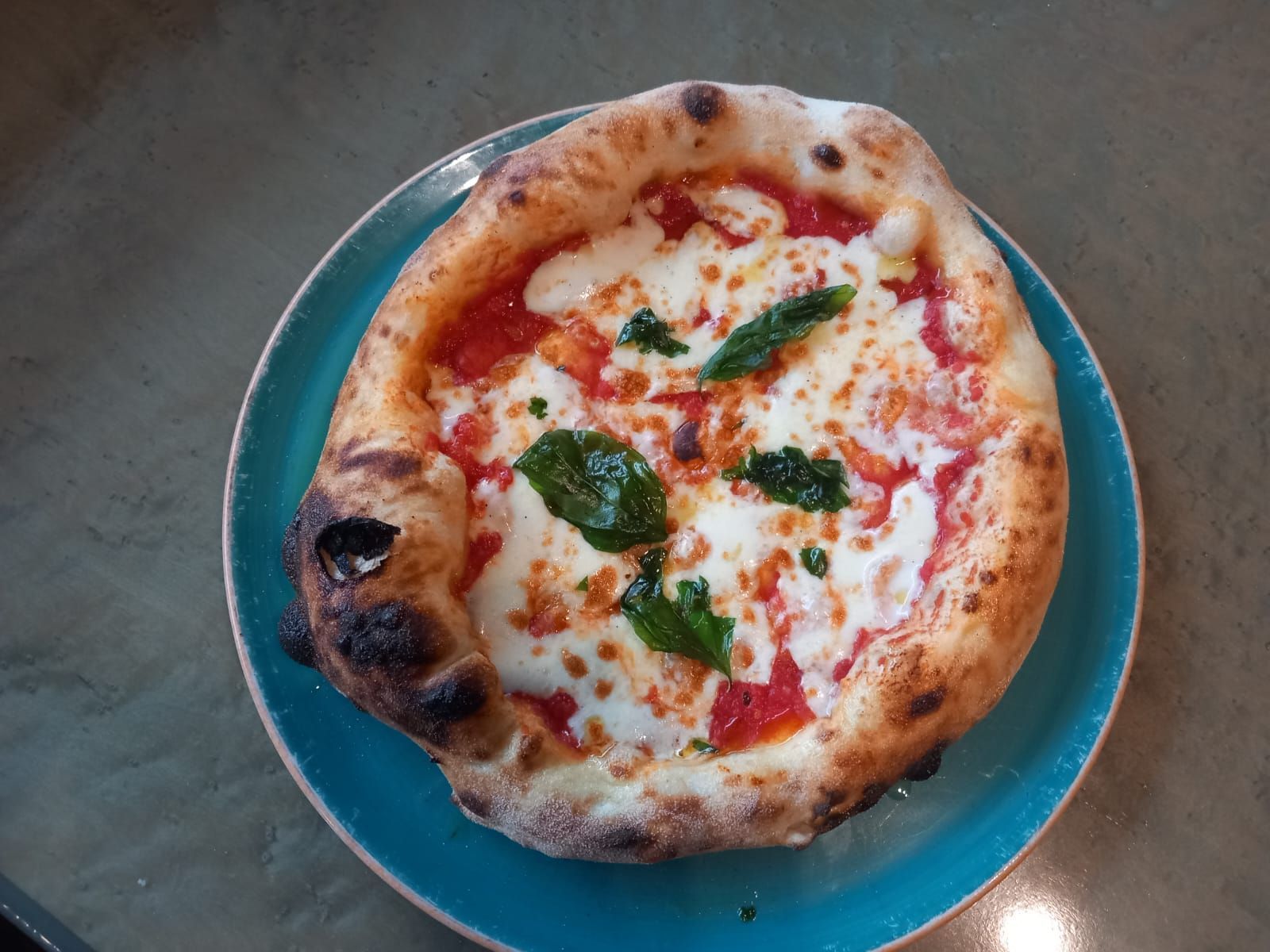 Una pizza è appoggiata su un piatto blu su un tavolo.