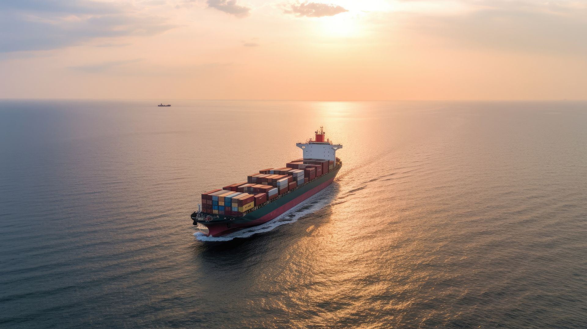 Un barco portacontenedores navega en el océano en calma durante la puesta de sol, transportando carga bajo un cielo dorado.