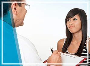 Un médico está hablando con una mujer joven que sostiene un portapapeles.