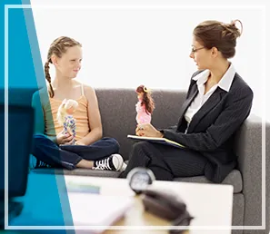 Una mujer está sentada en un sofá hablando con una niña que sostiene una muñeca.