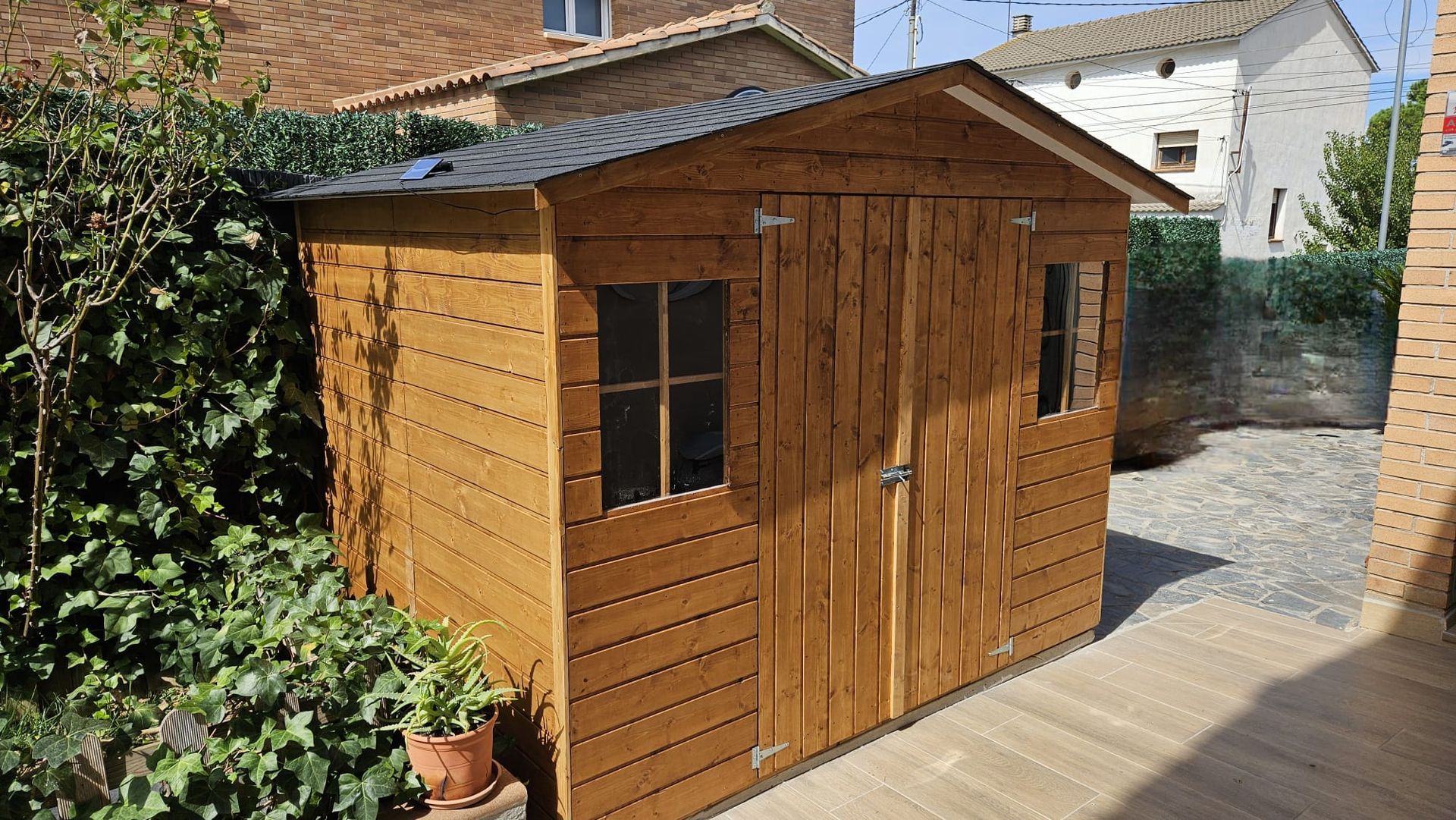 Un cobertizo de madera con techo negro está en un patio trasero.