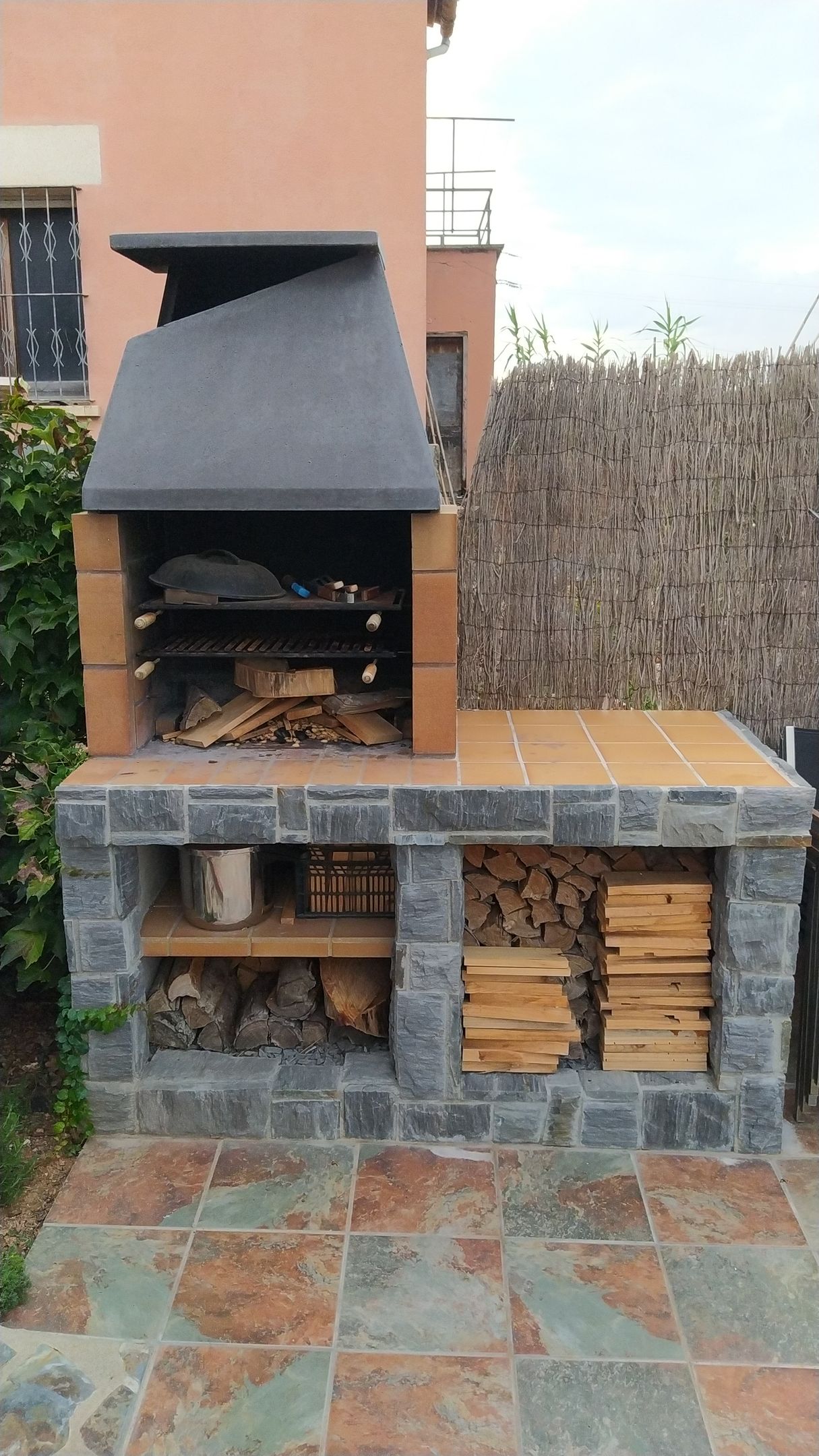 Una barbacoa de ladrillo con campana y pilas de leña delante de una casa.