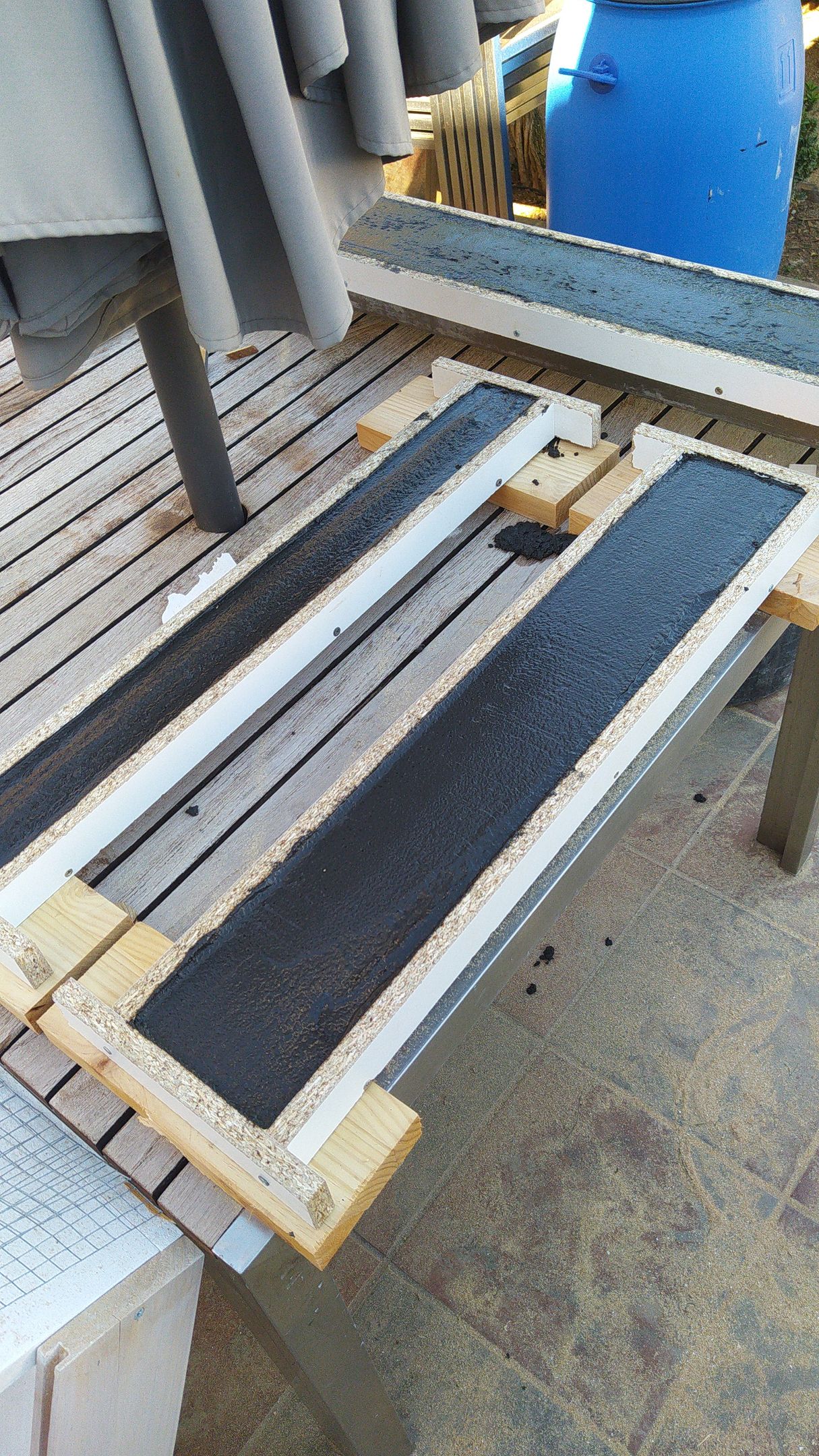 Un banco de madera está sentado encima de una mesa de madera al lado de un barril azul.