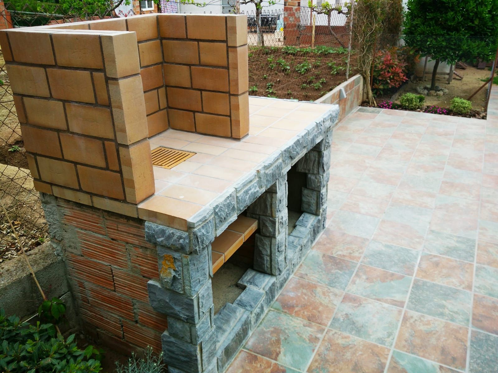 Una parrilla de ladrillos está colocada encima de un patio de baldosas.