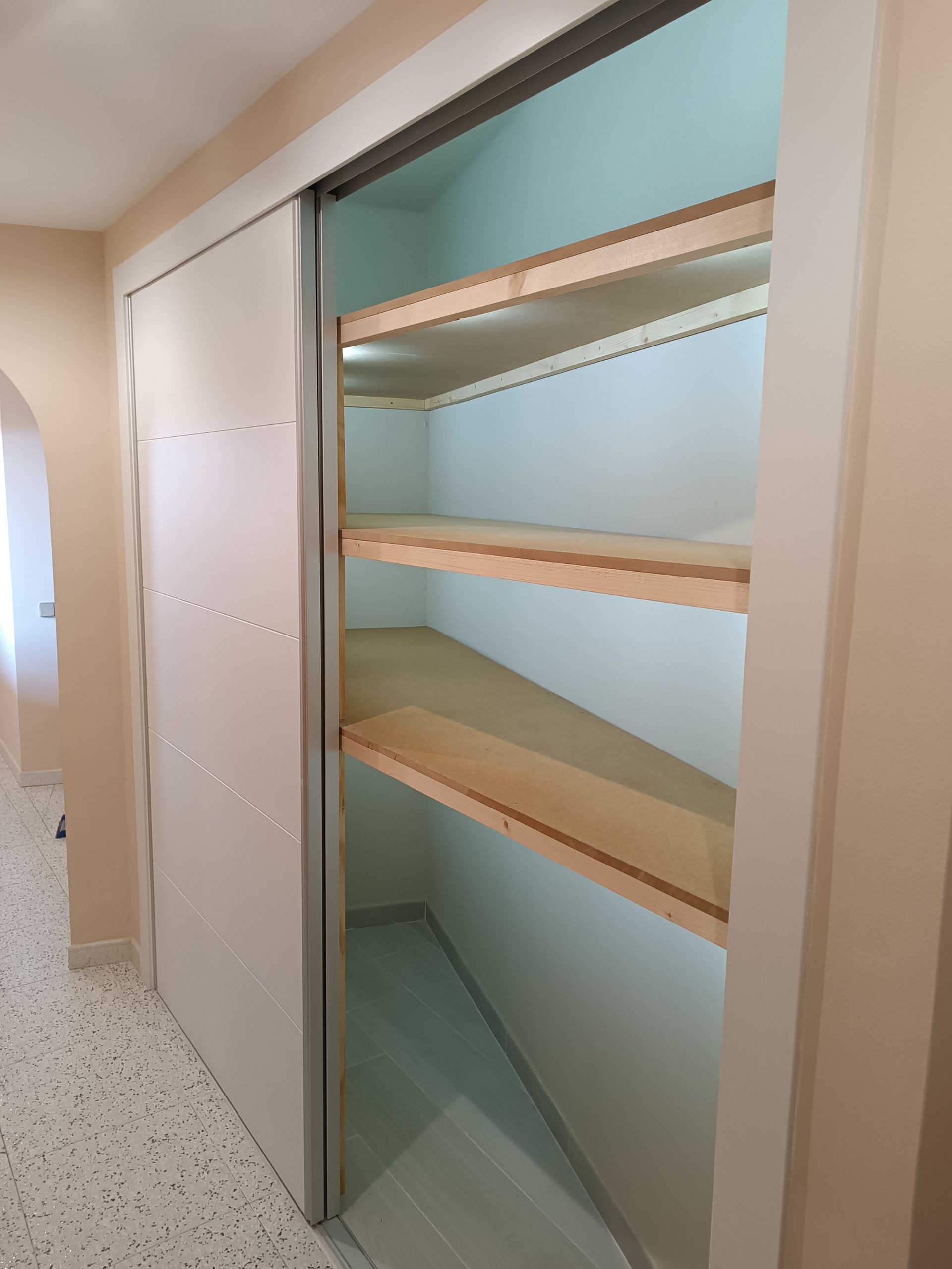 Un armario con puertas corredizas de vidrio y estantes de madera en un pasillo.